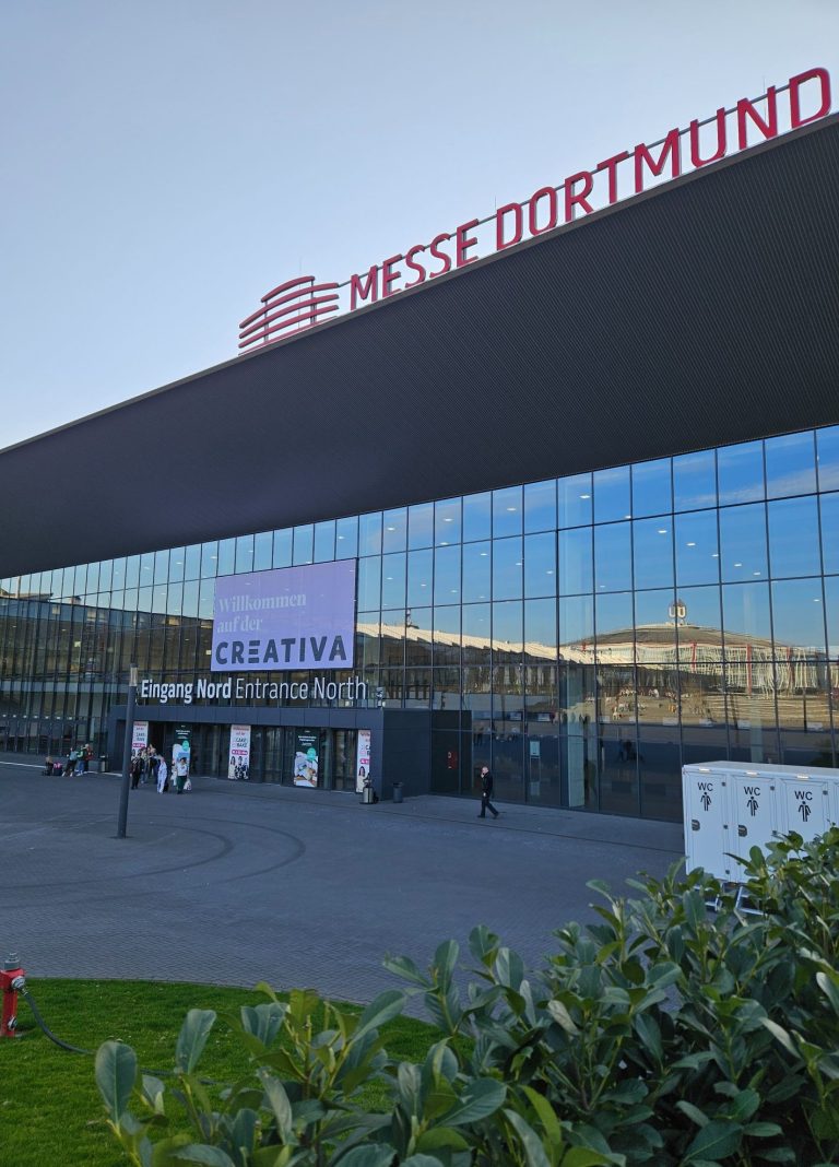 Eingang zur Messe Dortmund mit moderner Glasfassade und grüner Bepflanzung im Vordergrund.